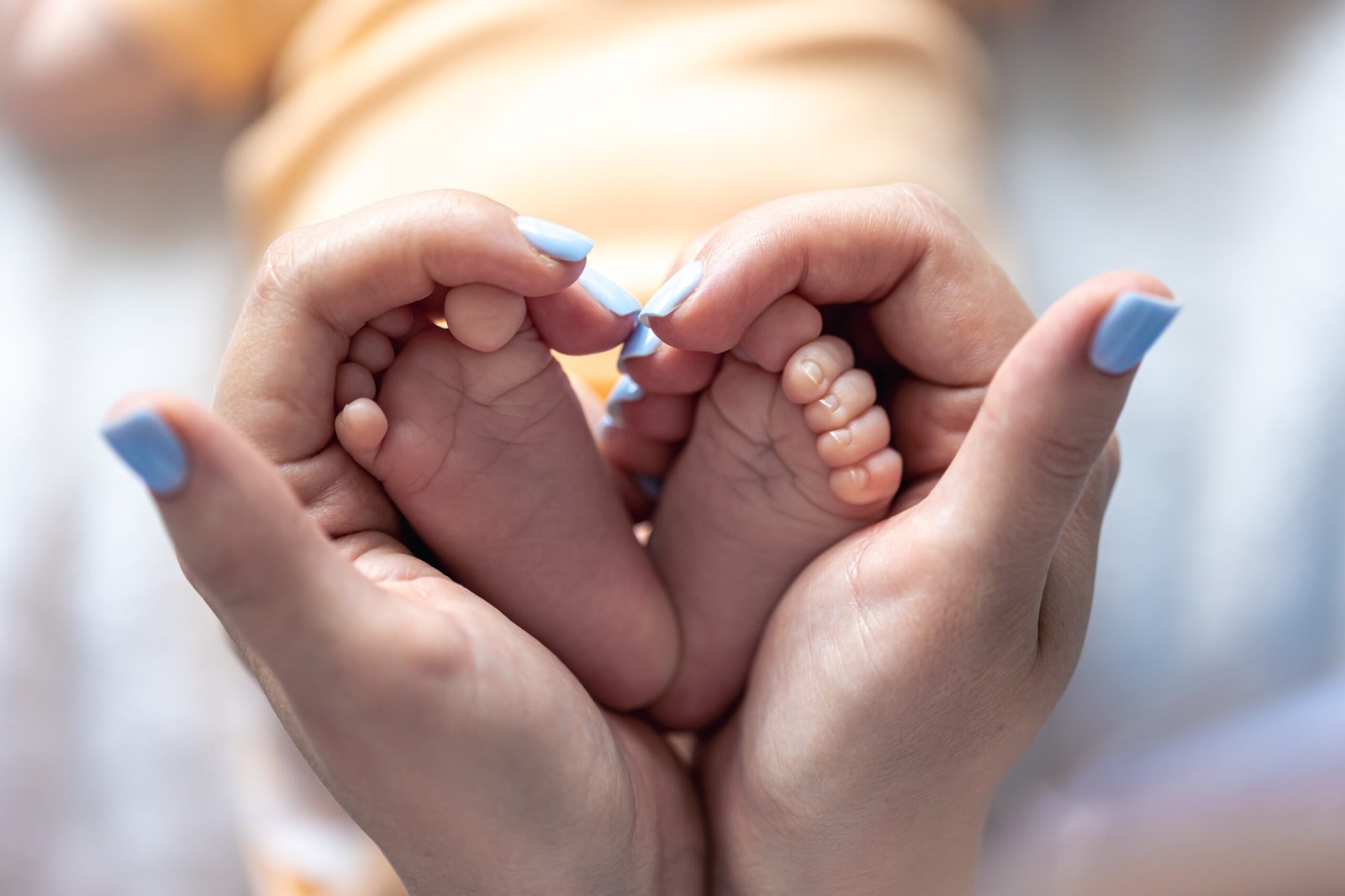 Mom holds the legs of a newborn baby in her hands, close-up, soft focus, concept of motherhood and care.